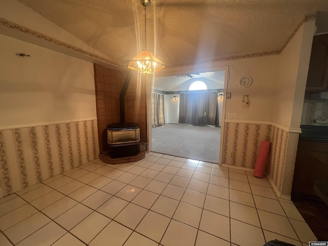 unfurnished dining area with a wood stove, light tile patterned floors, a textured ceiling, wainscoting, and lofted ceiling