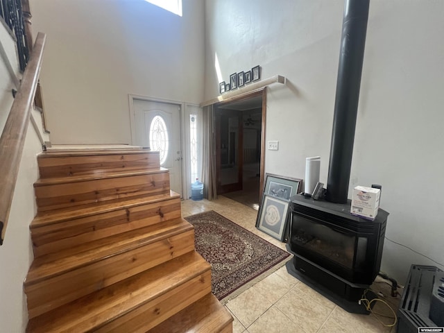 foyer featuring light tile patterned flooring, a high ceiling, a wood stove, and stairway