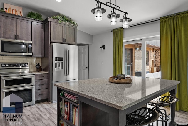 kitchen with dark brown cabinetry, tasteful backsplash, a breakfast bar, appliances with stainless steel finishes, and light wood finished floors