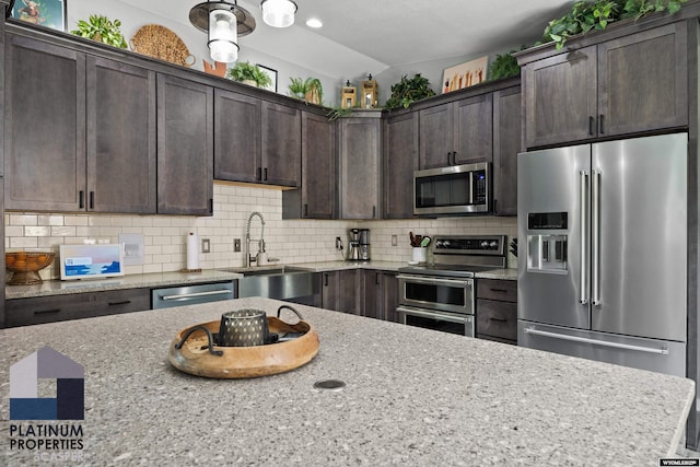 kitchen featuring a sink, appliances with stainless steel finishes, dark brown cabinetry, decorative backsplash, and light stone counters
