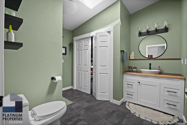bathroom featuring vanity, baseboards, a textured wall, a skylight, and wood finished floors
