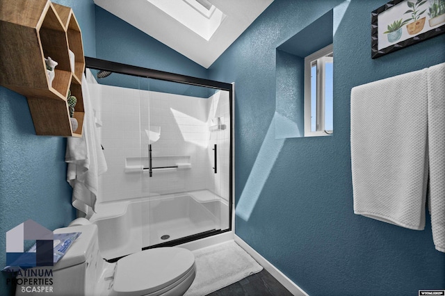 bathroom featuring baseboards, toilet, a textured wall, a skylight, and a stall shower