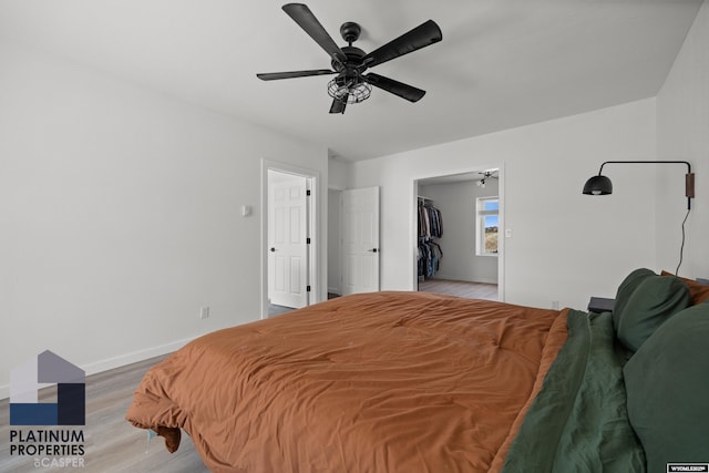 bedroom featuring light wood-type flooring, ceiling fan, baseboards, and a spacious closet