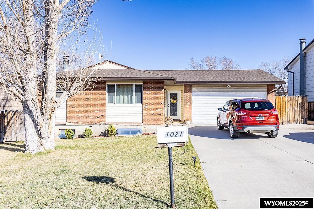 view of front of property featuring driveway, an attached garage, a front yard, brick siding, and fence