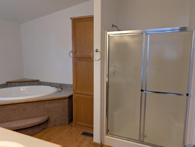 bathroom featuring wood finished floors, a bath, and a stall shower