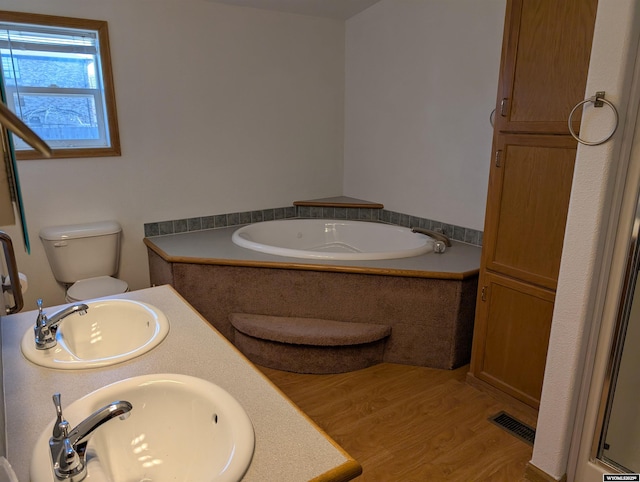 bathroom with a bath, a sink, wood finished floors, and visible vents