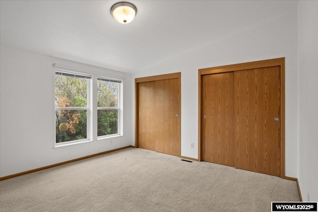 unfurnished bedroom featuring carpet flooring, two closets, visible vents, baseboards, and lofted ceiling