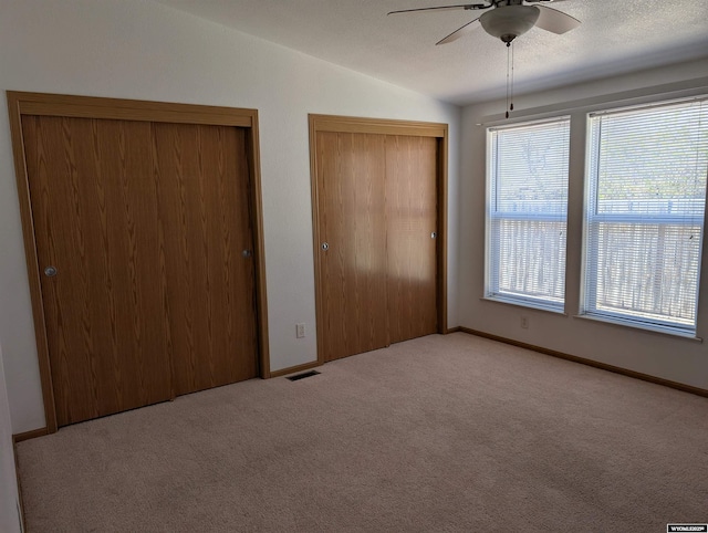 unfurnished bedroom with carpet flooring, visible vents, ceiling fan, vaulted ceiling, and two closets