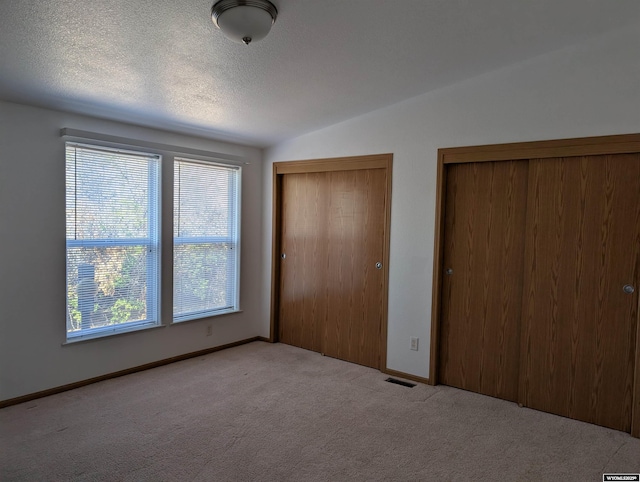 unfurnished bedroom featuring carpet, multiple windows, vaulted ceiling, and two closets