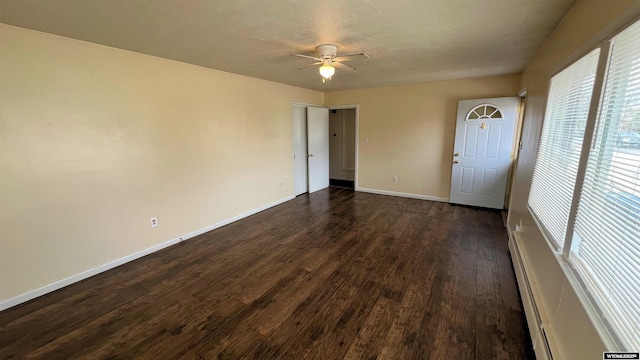 unfurnished room with baseboard heating, ceiling fan, baseboards, and dark wood-style floors
