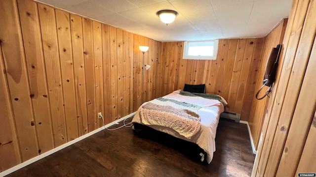 bedroom with a baseboard radiator, wooden walls, wood finished floors, and baseboards