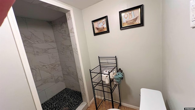 bathroom featuring toilet, baseboards, and a stall shower