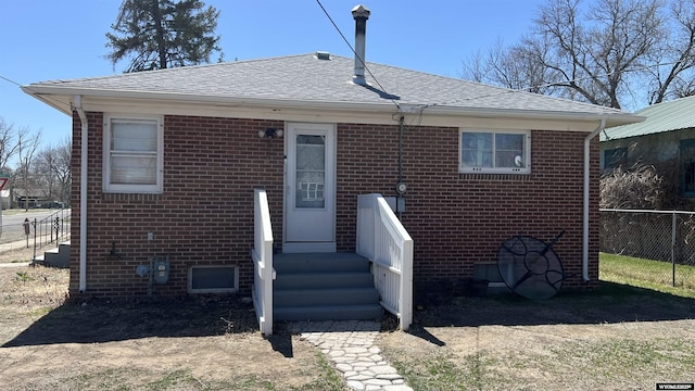 view of front facade with brick siding, a shingled roof, and fence