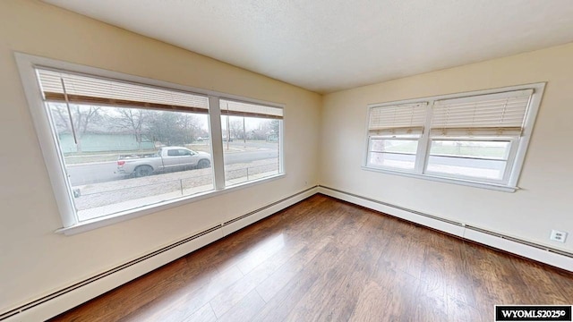 spare room featuring baseboard heating, a healthy amount of sunlight, and dark wood-style floors