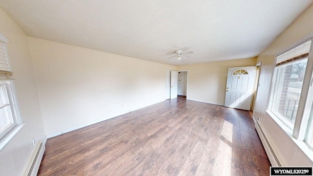 empty room featuring a baseboard heating unit, wood finished floors, and a wealth of natural light