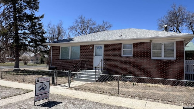 bungalow-style home with a gate, brick siding, roof with shingles, and a fenced front yard
