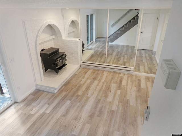 living area with a baseboard heating unit, wood finished floors, a wood stove, and stairs