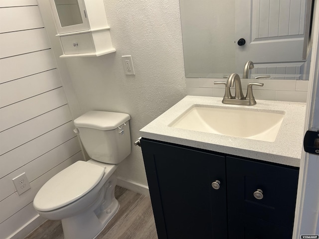 half bathroom with toilet, vanity, wood finished floors, and baseboards
