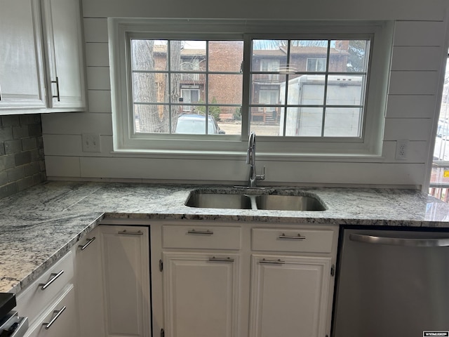 kitchen featuring white cabinets, decorative backsplash, stainless steel dishwasher, and a sink