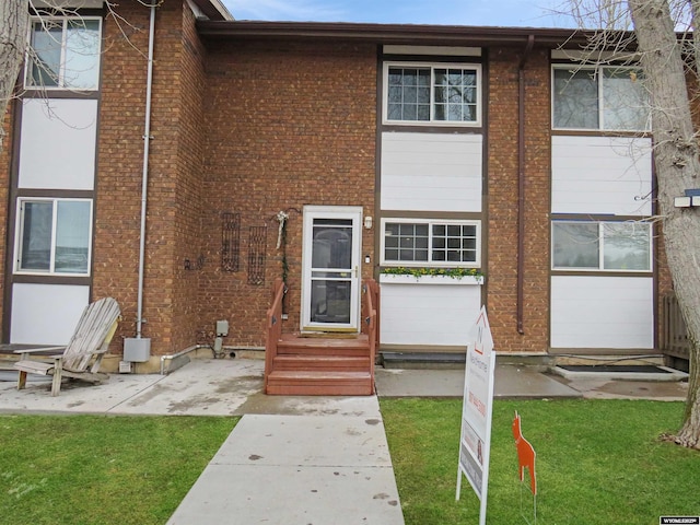 exterior space with brick siding, entry steps, and a front lawn