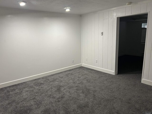 unfurnished room featuring wood walls, dark carpet, baseboards, and a textured ceiling
