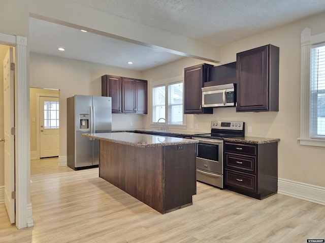 kitchen featuring a center island, a sink, stainless steel appliances, light wood finished floors, and baseboards