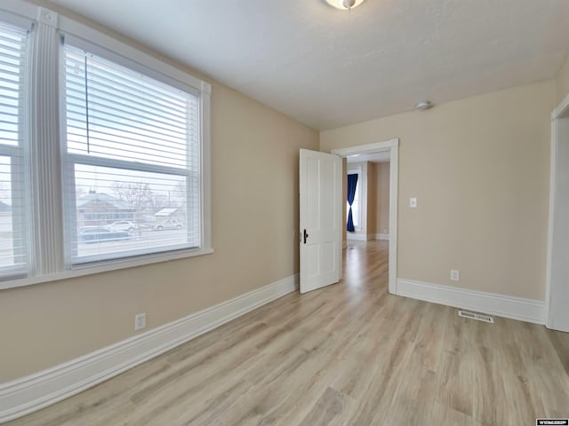 empty room featuring light wood-type flooring, visible vents, and baseboards