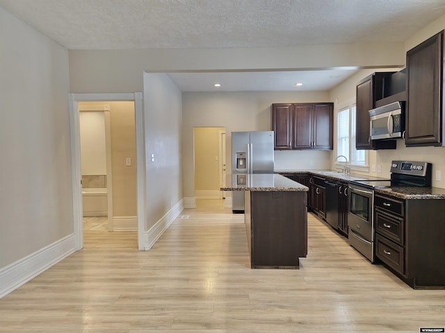 kitchen with light wood-type flooring, a kitchen island, appliances with stainless steel finishes, and a sink