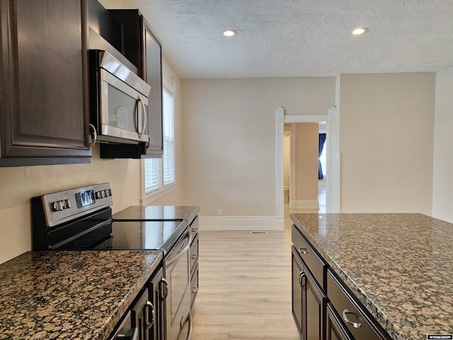 kitchen featuring stainless steel appliances, dark stone countertops, dark brown cabinets, light wood-style floors, and a textured ceiling