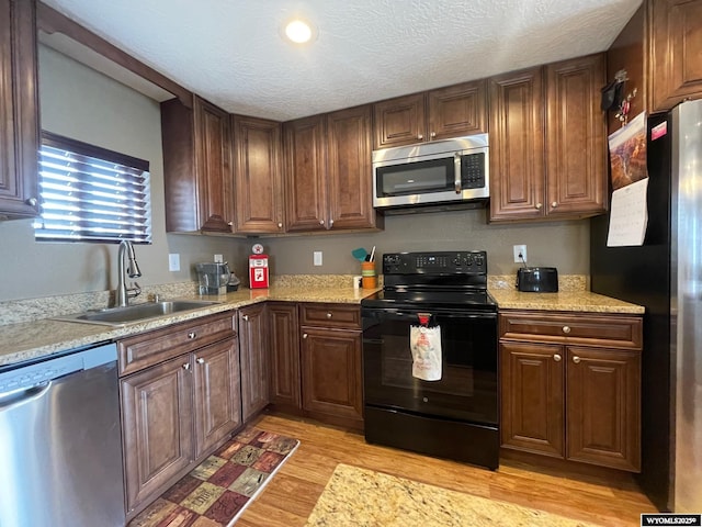 kitchen with light wood-style floors, a textured ceiling, stainless steel appliances, and a sink