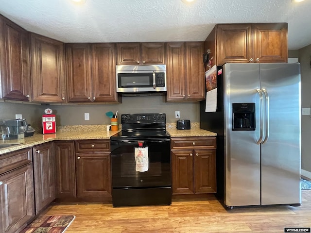 kitchen with light wood-type flooring, a textured ceiling, light stone countertops, and stainless steel appliances
