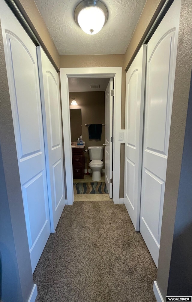 corridor featuring carpet floors, a textured ceiling, and visible vents