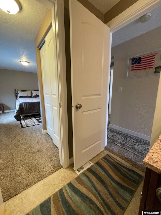 hall featuring a textured ceiling, baseboards, light carpet, and visible vents