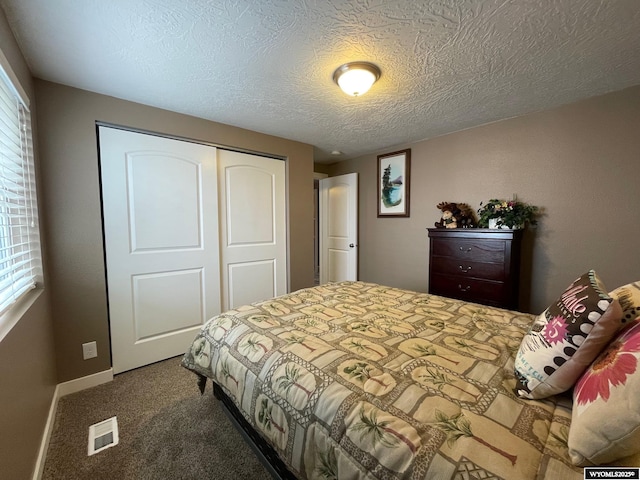 carpeted bedroom with baseboards, a textured ceiling, visible vents, and a closet