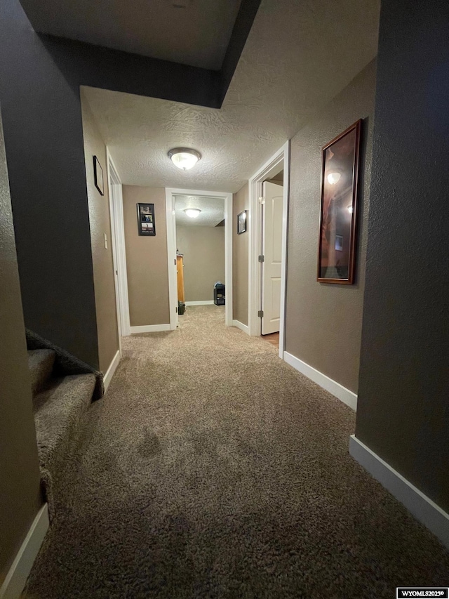 hallway with baseboards, carpet floors, and a textured ceiling