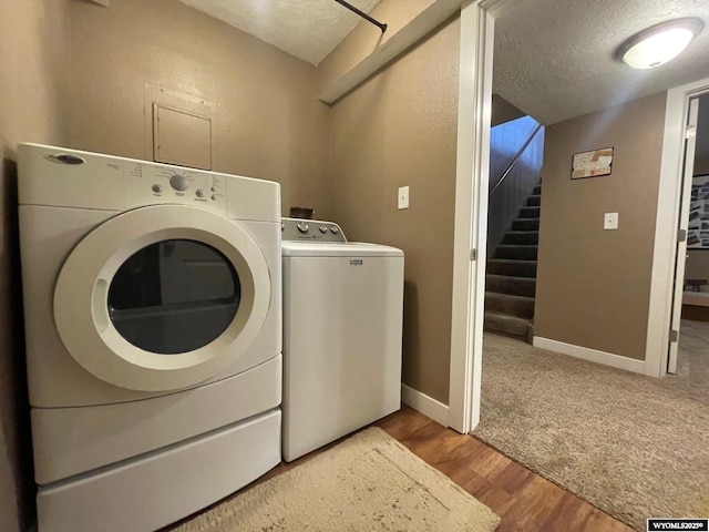clothes washing area with baseboards, wood finished floors, a textured ceiling, and independent washer and dryer