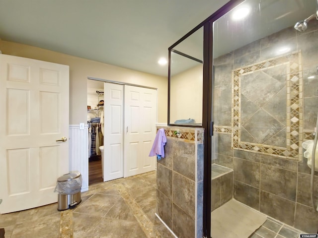 full bathroom with recessed lighting, a shower stall, a walk in closet, and wainscoting