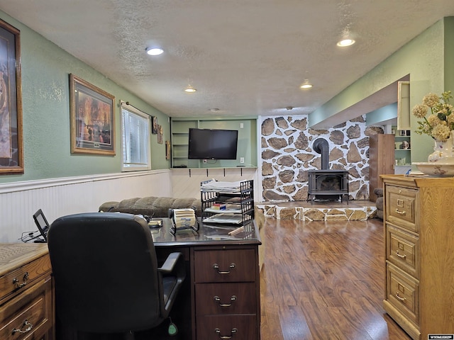 office space with recessed lighting, wood finished floors, a wood stove, wainscoting, and a textured ceiling