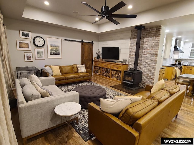 living room featuring light wood-type flooring, ceiling fan, a tray ceiling, and a wood stove