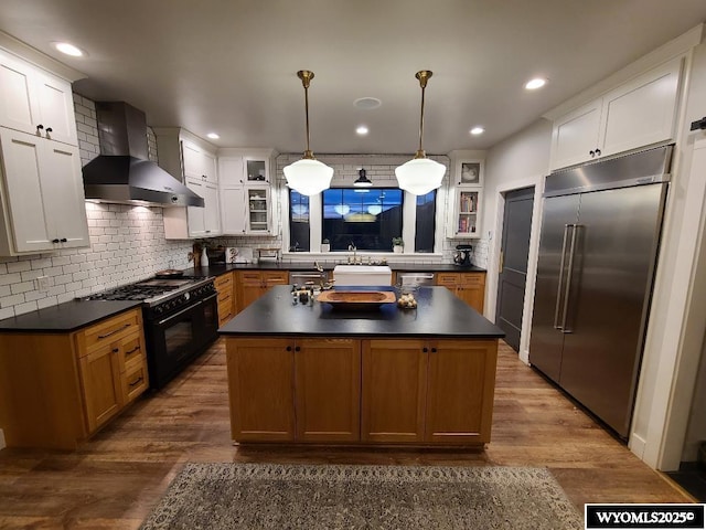 kitchen featuring backsplash, dark countertops, wall chimney exhaust hood, and stainless steel appliances