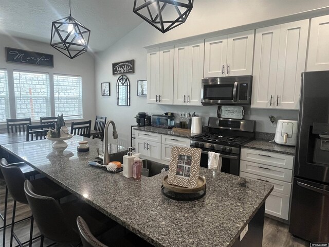 640 Lynn Ct, Green River, WY 82935 - kitchen featuring dark wood-style floors, vaulted ceiling, appliances with stainless steel finishes, a breakfast bar area, and white cabinetry