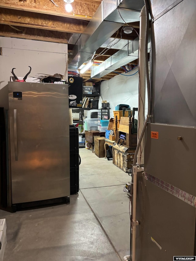 unfinished basement with heating unit and freestanding refrigerator