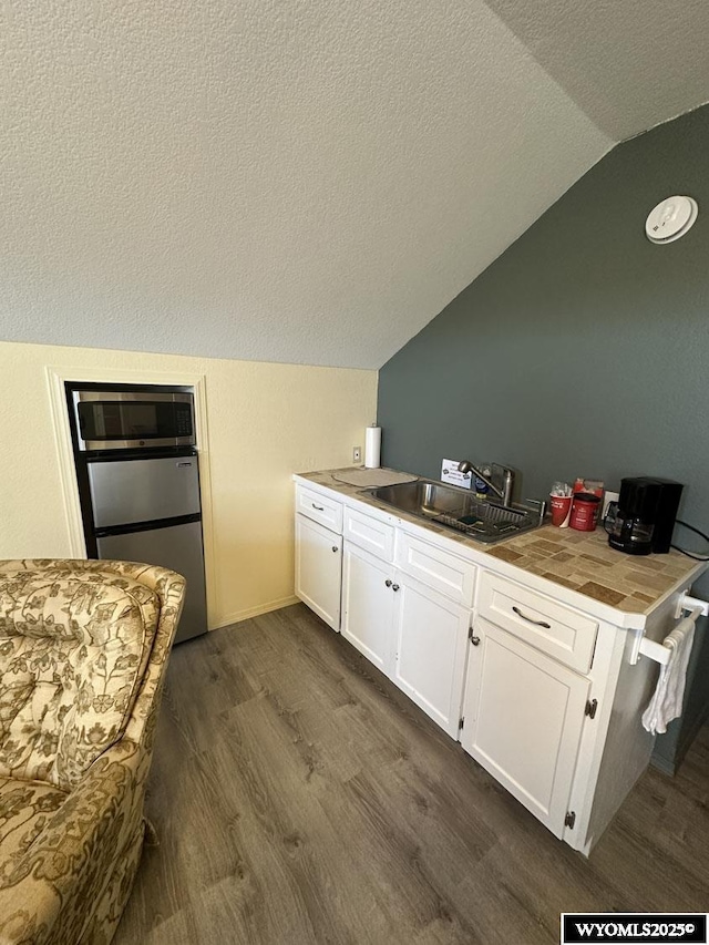 kitchen featuring a textured ceiling, vaulted ceiling, white cabinetry, dark wood-type flooring, and appliances with stainless steel finishes
