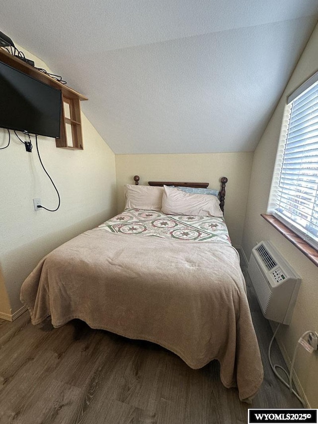 bedroom featuring a wall mounted AC, wood finished floors, baseboards, and vaulted ceiling