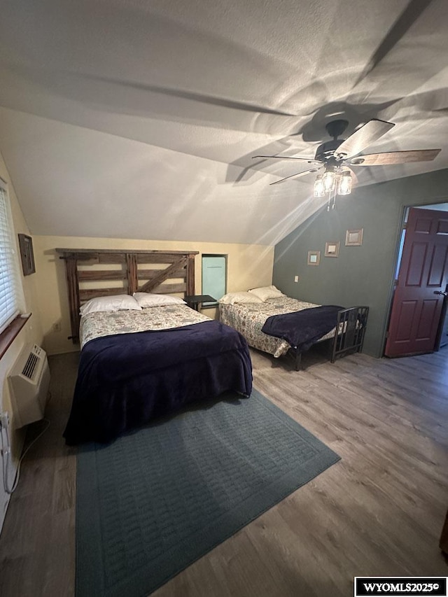 bedroom with ceiling fan, vaulted ceiling, a wall unit AC, and wood finished floors