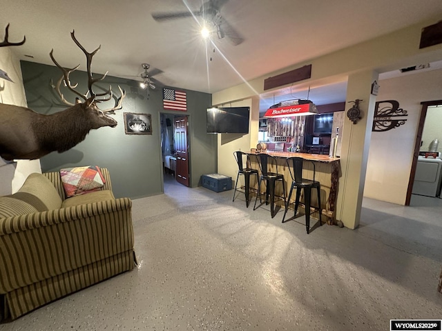 interior space featuring speckled floor, a dry bar, ceiling fan, and washer / clothes dryer