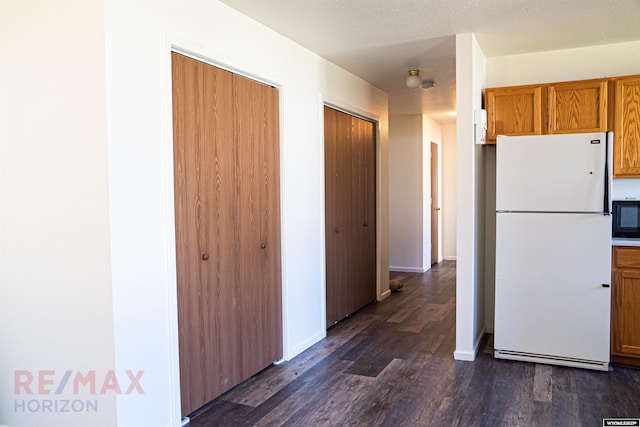 kitchen featuring dark wood-type flooring, freestanding refrigerator, baseboards, and brown cabinets