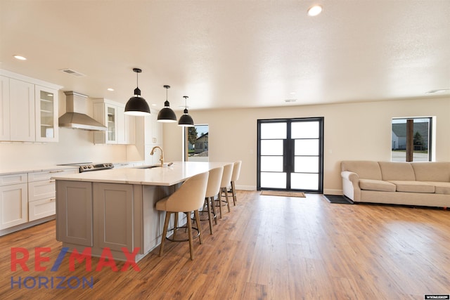 kitchen with white cabinets, visible vents, wall chimney exhaust hood, a center island with sink, and a breakfast bar area