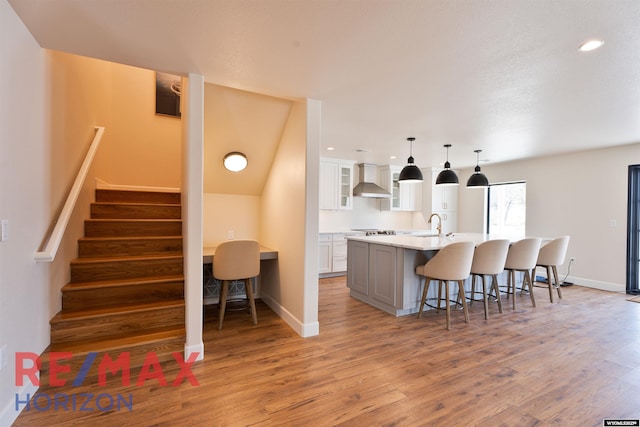 kitchen with an island with sink, a breakfast bar, light wood-type flooring, wall chimney exhaust hood, and white cabinetry