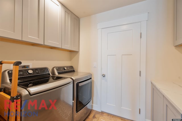 clothes washing area featuring washing machine and dryer, light wood-style floors, and cabinet space